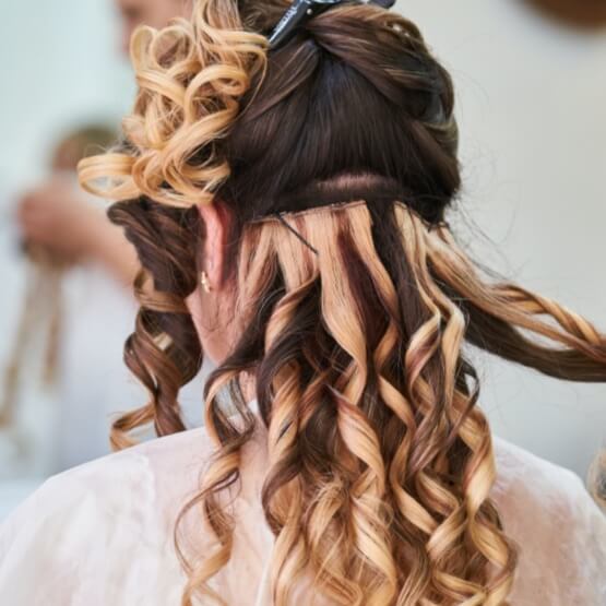 Eine Nahaufnahme von Haarverlängerungen bei einer Frau mit lockigen Haaren, die professionell gestylt werden.