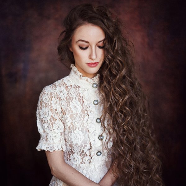 Porträt einer Frau mit langen, welligen Haaren, die ein elegantes Spitzenkleid trägt. Das Bild zeigt ihre natürliche Schönheit und das sorgfältige Haarstyling von Get Your Look in Frankfurt. Copyright by Get Your Look.