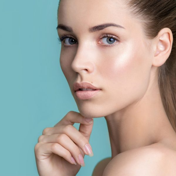 Porträt einer jungen Frau mit makelloser Haut und dezentem Make-up vor einem blauen Hintergrund. Das Bild zeigt die professionelle Make-up-Arbeit von Get Your Look in Frankfurt. Copyright by Get Your Look.